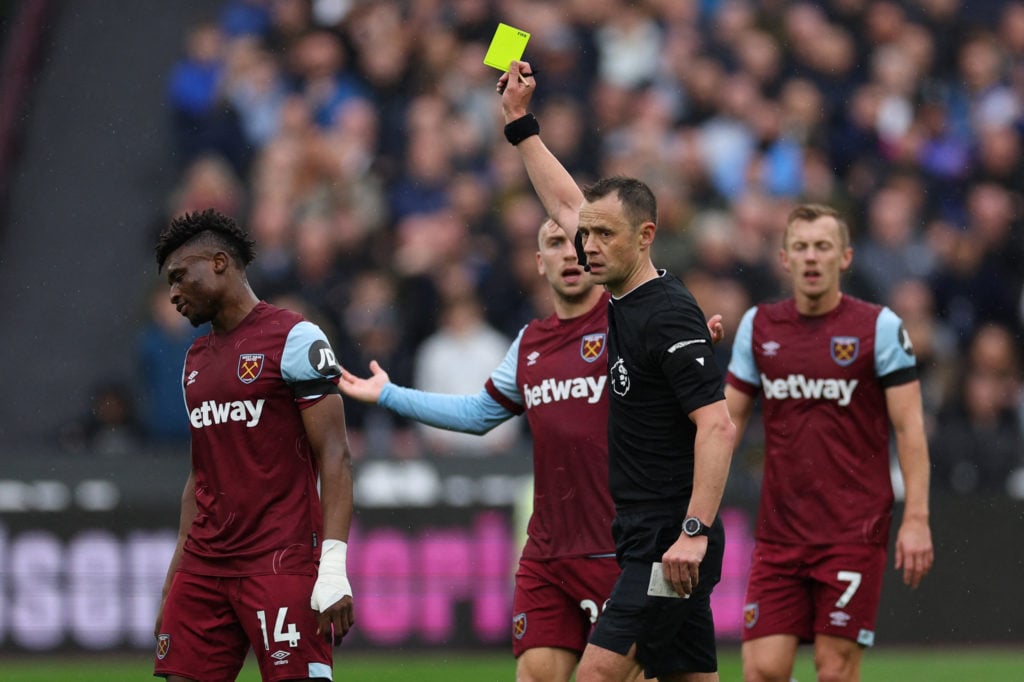 English referee Stuart Attwell shows a yellow card to West Ham United's Ghanaian midfielder #14 Mohammad Kudas (L) during the English Premier Leagu...